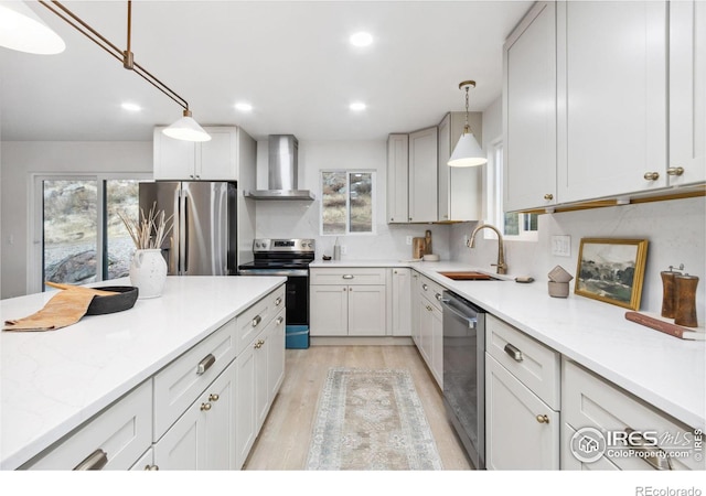 kitchen with pendant lighting, sink, wall chimney exhaust hood, appliances with stainless steel finishes, and white cabinetry