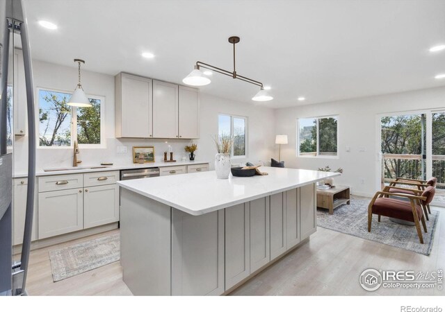 kitchen with backsplash, sink, light hardwood / wood-style floors, a kitchen island, and hanging light fixtures