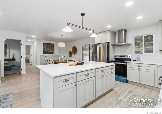 kitchen featuring wall chimney exhaust hood, stainless steel appliances, white cabinets, a center island, and hanging light fixtures