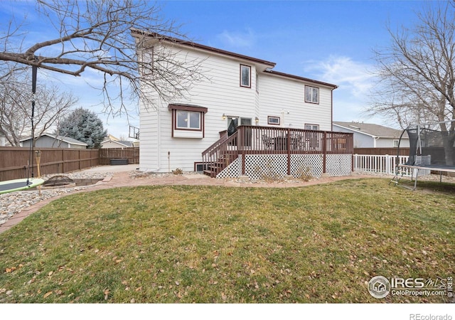 rear view of property with a wooden deck, a trampoline, and a lawn