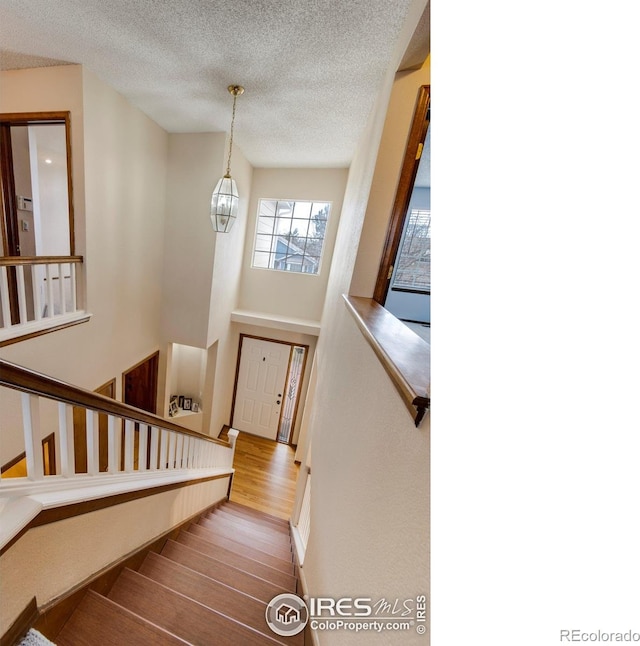 staircase with a chandelier, a textured ceiling, and hardwood / wood-style flooring