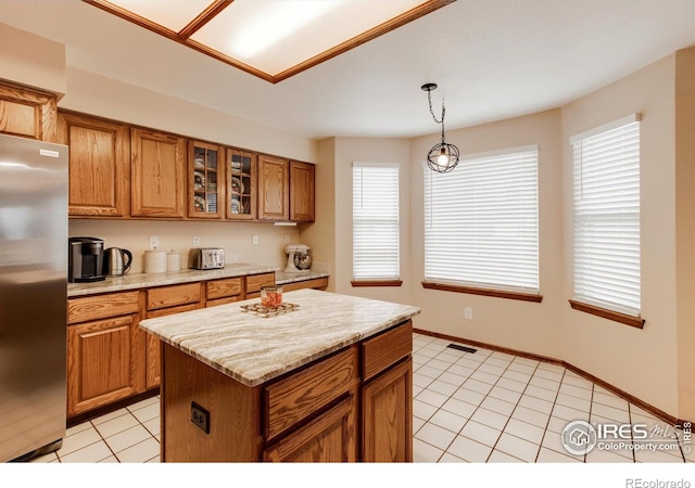 kitchen featuring a center island, a healthy amount of sunlight, hanging light fixtures, stainless steel fridge, and light tile patterned flooring