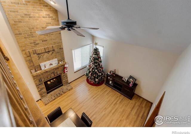 living room with a brick fireplace, a textured ceiling, ceiling fan, hardwood / wood-style floors, and lofted ceiling