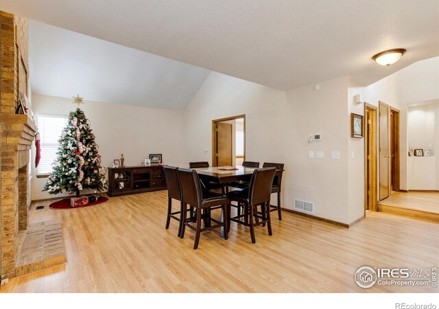 dining area with a fireplace, hardwood / wood-style floors, and vaulted ceiling