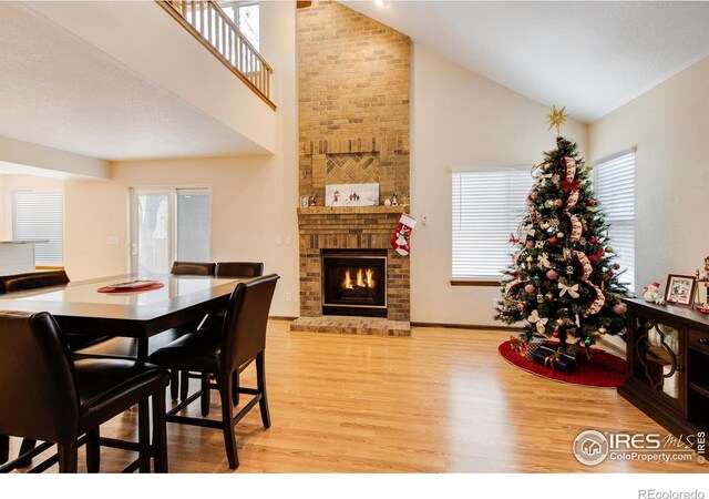 dining area with light hardwood / wood-style flooring, high vaulted ceiling, and a brick fireplace