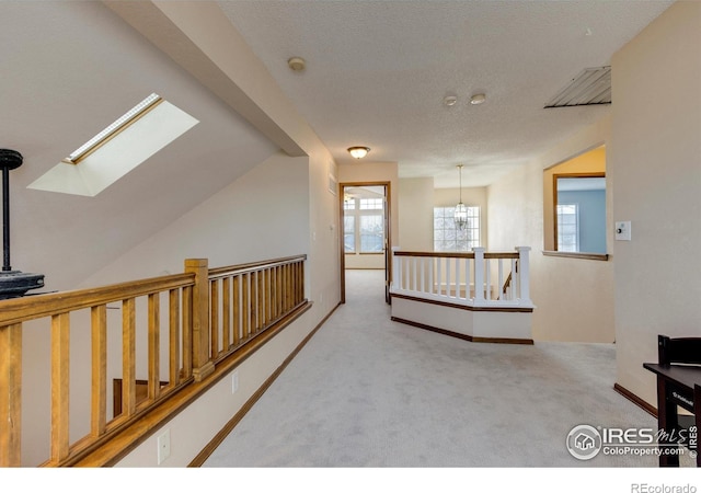 hallway with vaulted ceiling with skylight, light colored carpet, a textured ceiling, and an inviting chandelier