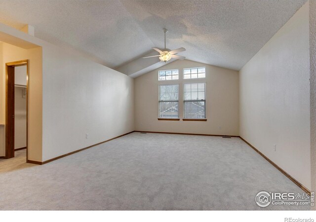 carpeted spare room with a textured ceiling, vaulted ceiling, and ceiling fan