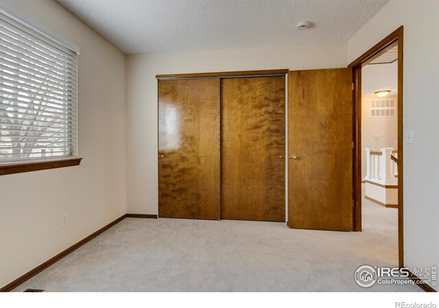 unfurnished bedroom with light colored carpet, a textured ceiling, and a closet