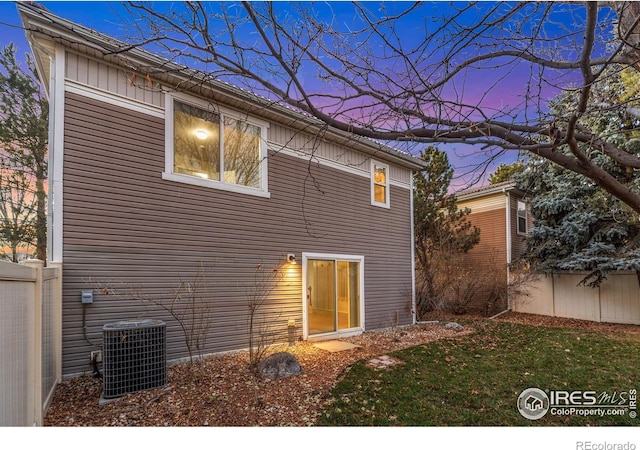 back house at dusk featuring central AC unit and a yard