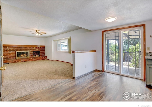 unfurnished living room with carpet flooring, ceiling fan, a fireplace, and a textured ceiling