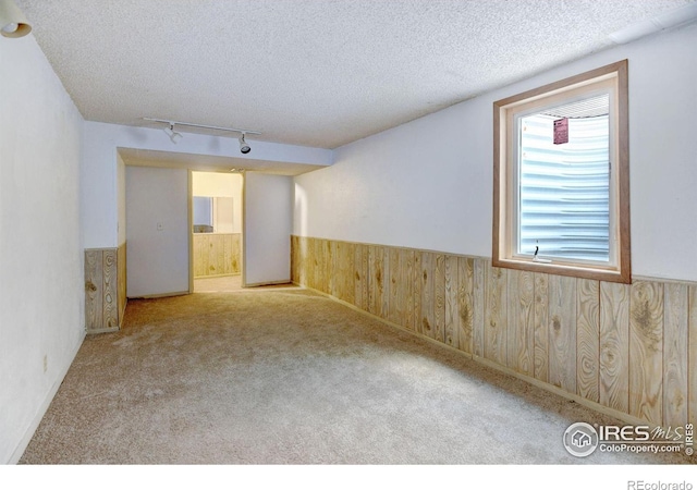 carpeted spare room with wood walls, a textured ceiling, and track lighting