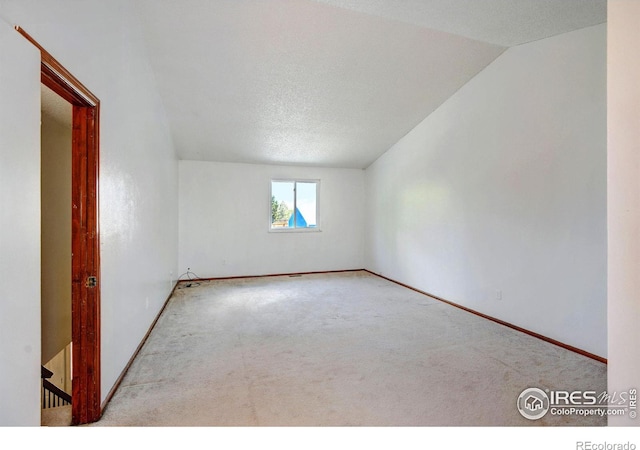 carpeted spare room featuring a textured ceiling and vaulted ceiling