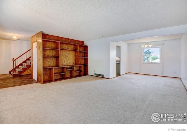 unfurnished living room featuring a chandelier, carpet, and a textured ceiling