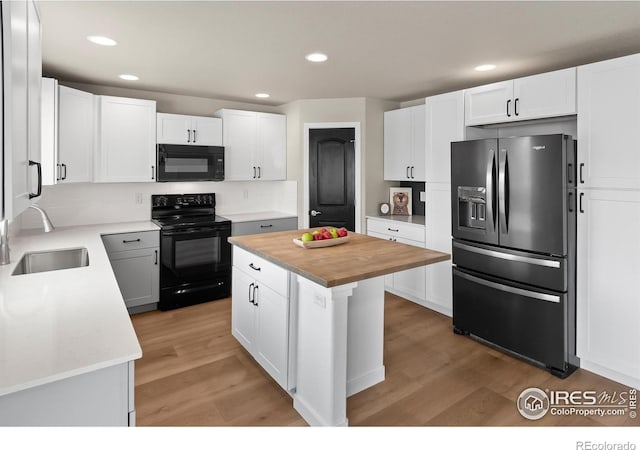 kitchen featuring light hardwood / wood-style flooring, black appliances, a kitchen island, white cabinets, and sink