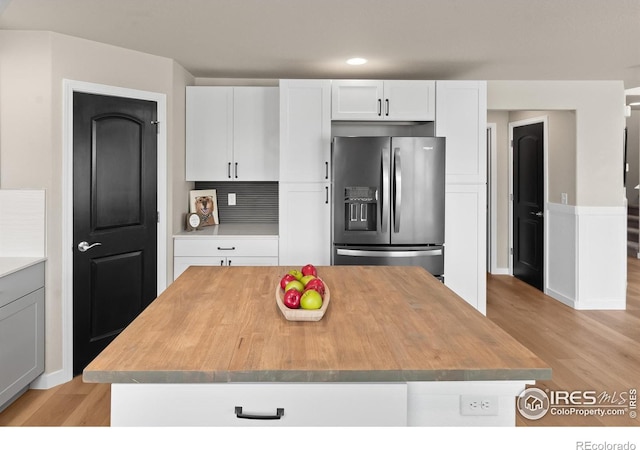 kitchen with light hardwood / wood-style floors, a kitchen island, decorative backsplash, stainless steel refrigerator with ice dispenser, and white cabinetry