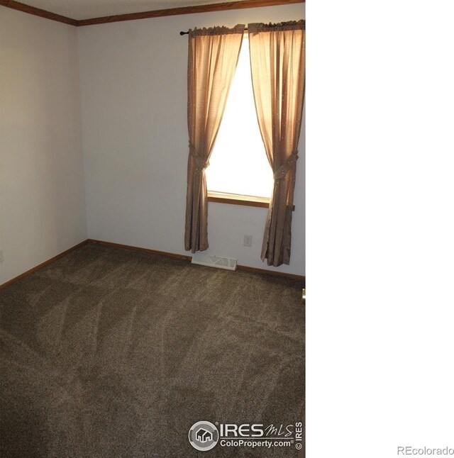 empty room featuring ornamental molding, dark colored carpet, and visible vents