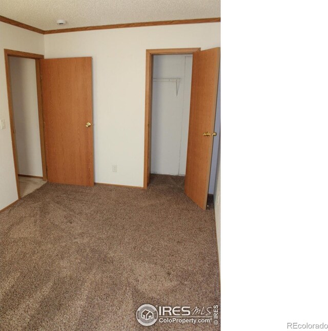 unfurnished bedroom featuring a textured ceiling, ornamental molding, a closet, and carpet