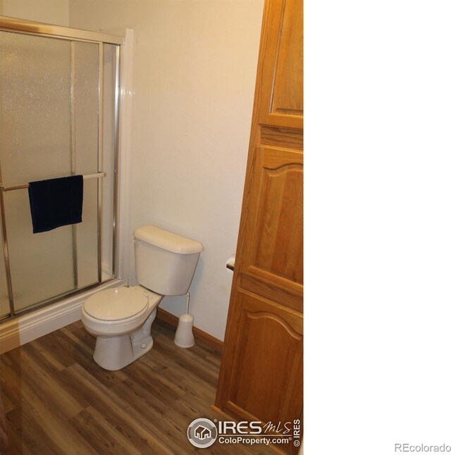 bathroom with a stall shower, toilet, and wood finished floors