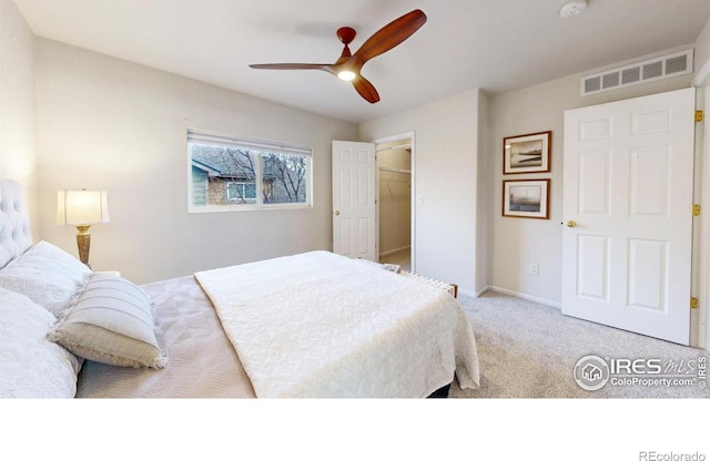 carpeted bedroom with a walk in closet and ceiling fan