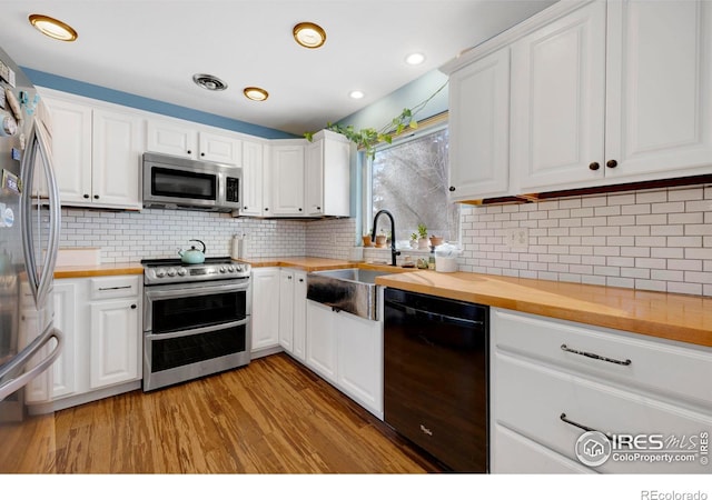 kitchen featuring backsplash, stainless steel appliances, sink, white cabinets, and butcher block counters