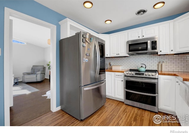 kitchen featuring white cabinets, decorative backsplash, butcher block counters, and appliances with stainless steel finishes