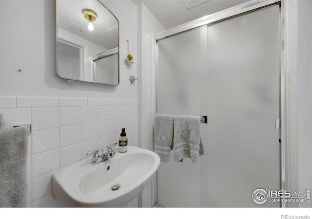 bathroom with sink, a shower with shower door, and tile walls