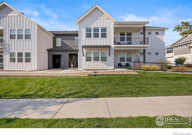 view of front of home with board and batten siding, a front yard, fence, and a balcony