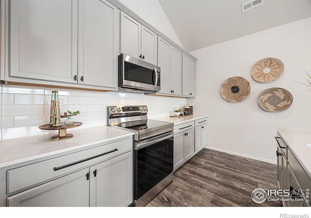 kitchen with gray cabinetry, dark wood-type flooring, stainless steel appliances, vaulted ceiling, and decorative backsplash