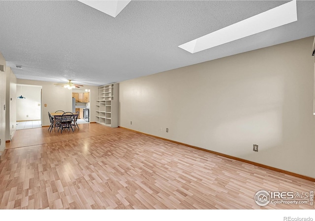 interior space featuring built in shelves, ceiling fan, a skylight, a textured ceiling, and light wood-type flooring