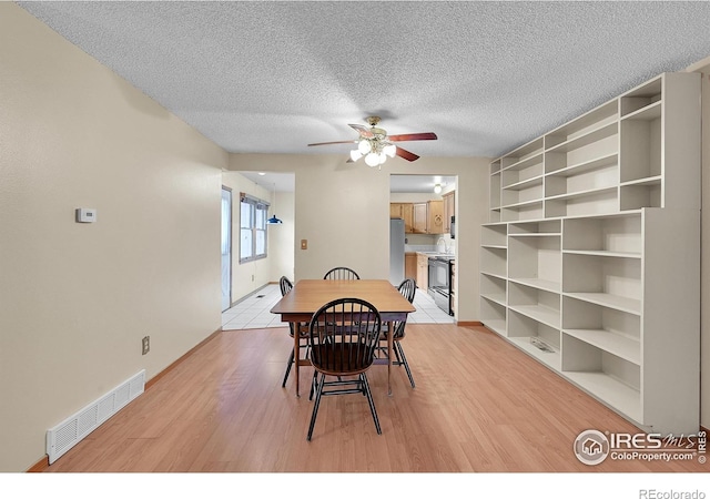 dining area featuring ceiling fan, light wood-type flooring, and a textured ceiling