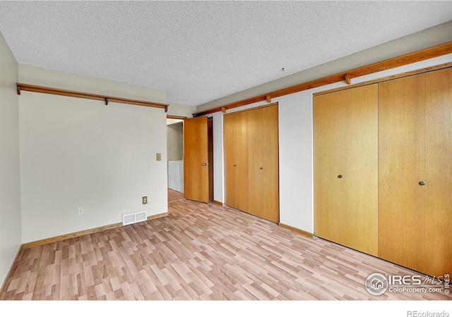 unfurnished bedroom featuring light wood-type flooring, a textured ceiling, and multiple closets