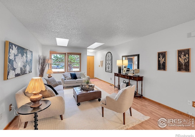 living area with a textured ceiling, light wood-type flooring, a skylight, and baseboards