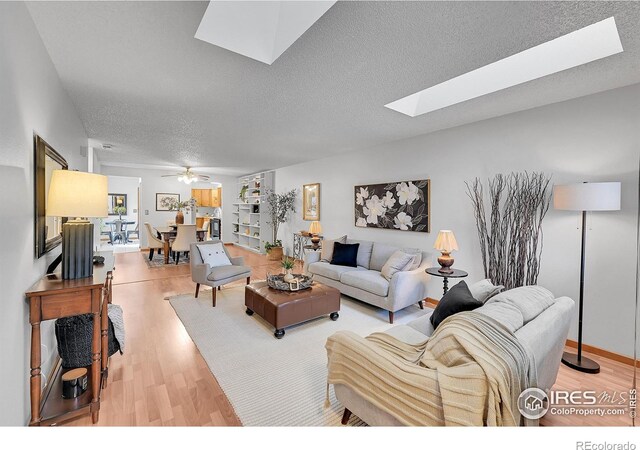 living room with a ceiling fan, a skylight, a textured ceiling, and light wood finished floors