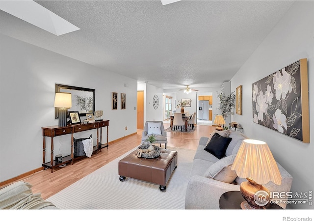 living area with a textured ceiling, a skylight, wood finished floors, a ceiling fan, and baseboards