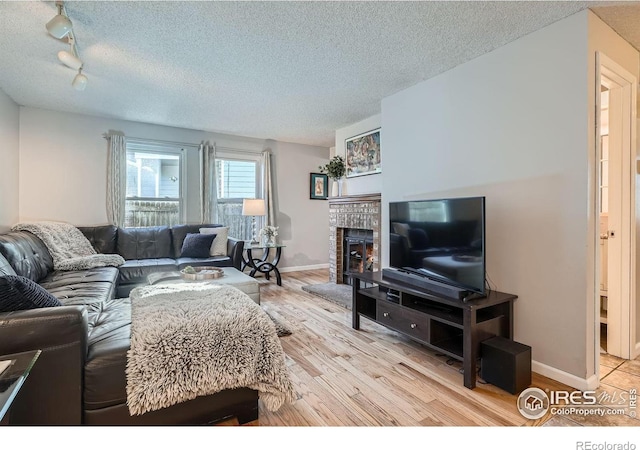 living room with a textured ceiling, light wood-type flooring, rail lighting, and a brick fireplace