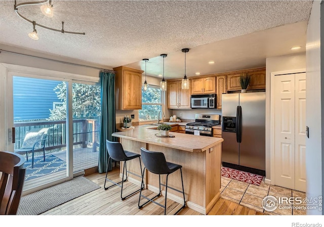 kitchen featuring pendant lighting, a kitchen bar, a textured ceiling, and appliances with stainless steel finishes