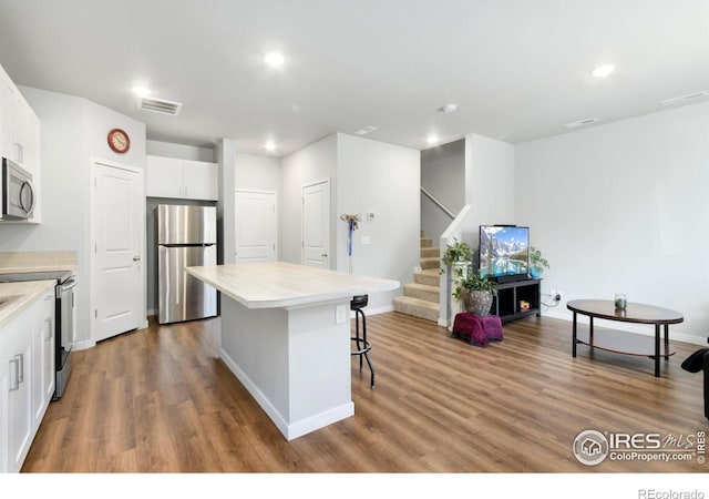 kitchen featuring stainless steel appliances, a kitchen island, hardwood / wood-style floors, a breakfast bar, and white cabinets