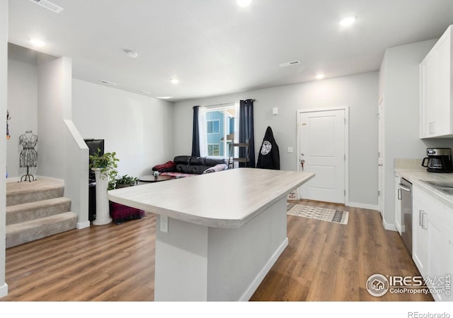 kitchen with white cabinets, hardwood / wood-style floors, a kitchen island, and stainless steel dishwasher