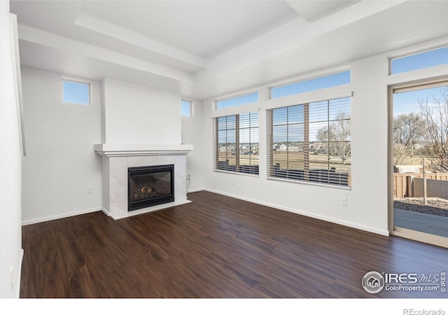 unfurnished living room featuring a raised ceiling, dark wood-type flooring, and a tiled fireplace