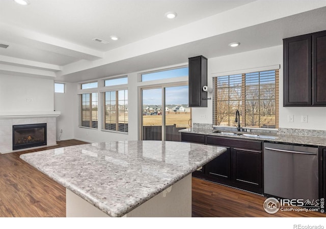 kitchen featuring light stone counters, sink, dishwasher, a kitchen island, and a tiled fireplace