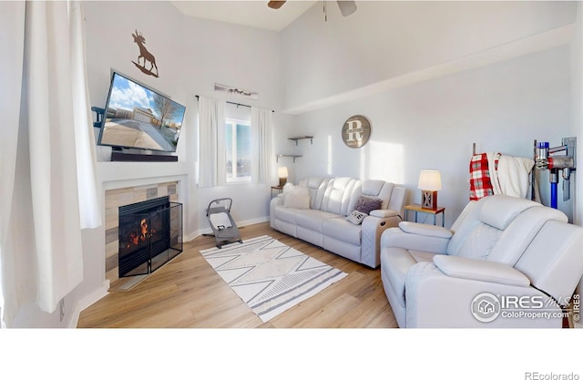 living room featuring light hardwood / wood-style flooring, ceiling fan, and a tiled fireplace