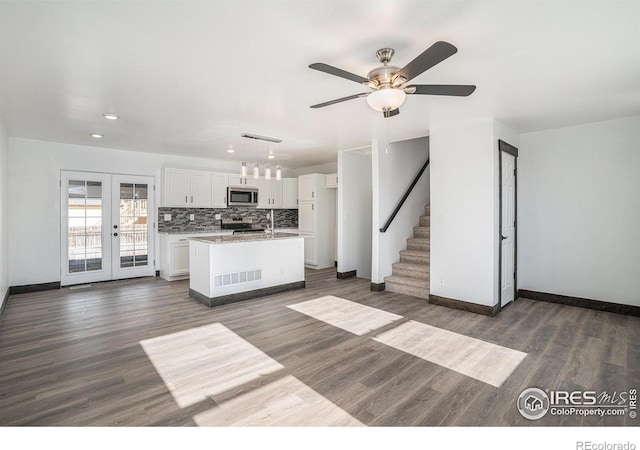 kitchen featuring appliances with stainless steel finishes, french doors, decorative light fixtures, white cabinetry, and an island with sink