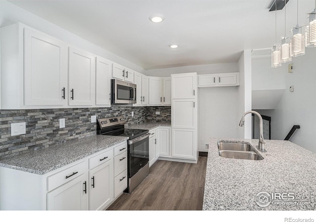 kitchen featuring hanging light fixtures, sink, appliances with stainless steel finishes, light stone counters, and white cabinetry