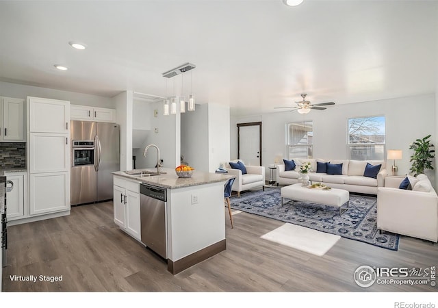 kitchen featuring stainless steel appliances, a kitchen island with sink, sink, decorative light fixtures, and white cabinetry