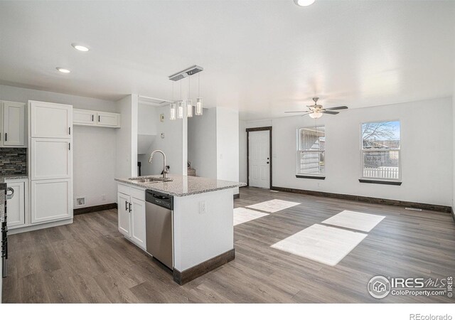 kitchen featuring stainless steel dishwasher, sink, pendant lighting, a center island with sink, and white cabinets