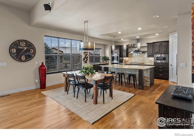 dining space with light wood-type flooring, a tray ceiling, and sink