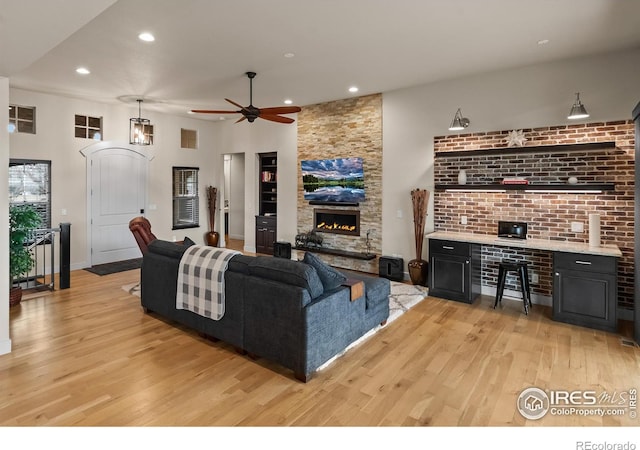 living room with a stone fireplace, ceiling fan, and light wood-type flooring