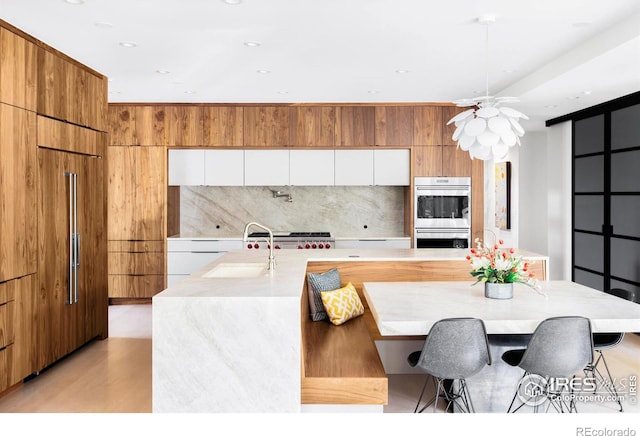 kitchen with white cabinetry, a kitchen bar, stainless steel double oven, and a large island with sink