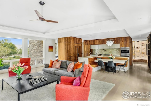 living room with light hardwood / wood-style floors, a raised ceiling, and ceiling fan