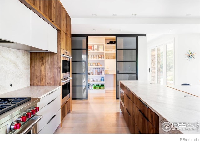 kitchen with backsplash, white cabinetry, stainless steel appliances, and light hardwood / wood-style floors